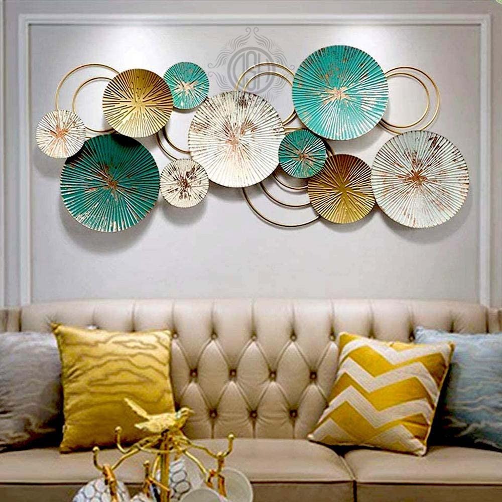 Decorative wall art with circular metal plates in teal, gold, and white above a beige sofa with colorful cushions.

