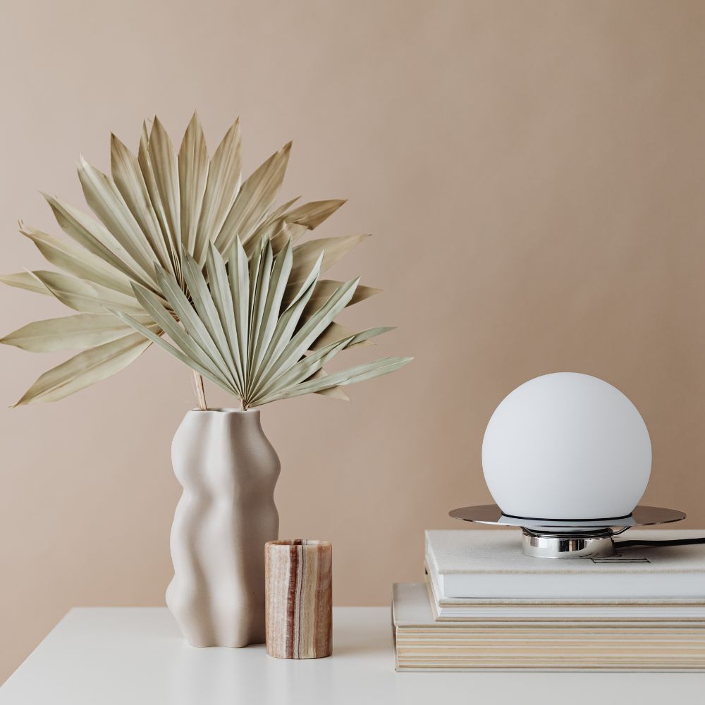 Decorative items including a vase with dried leaves, a small candle, and a spherical lamp on a beige background.


