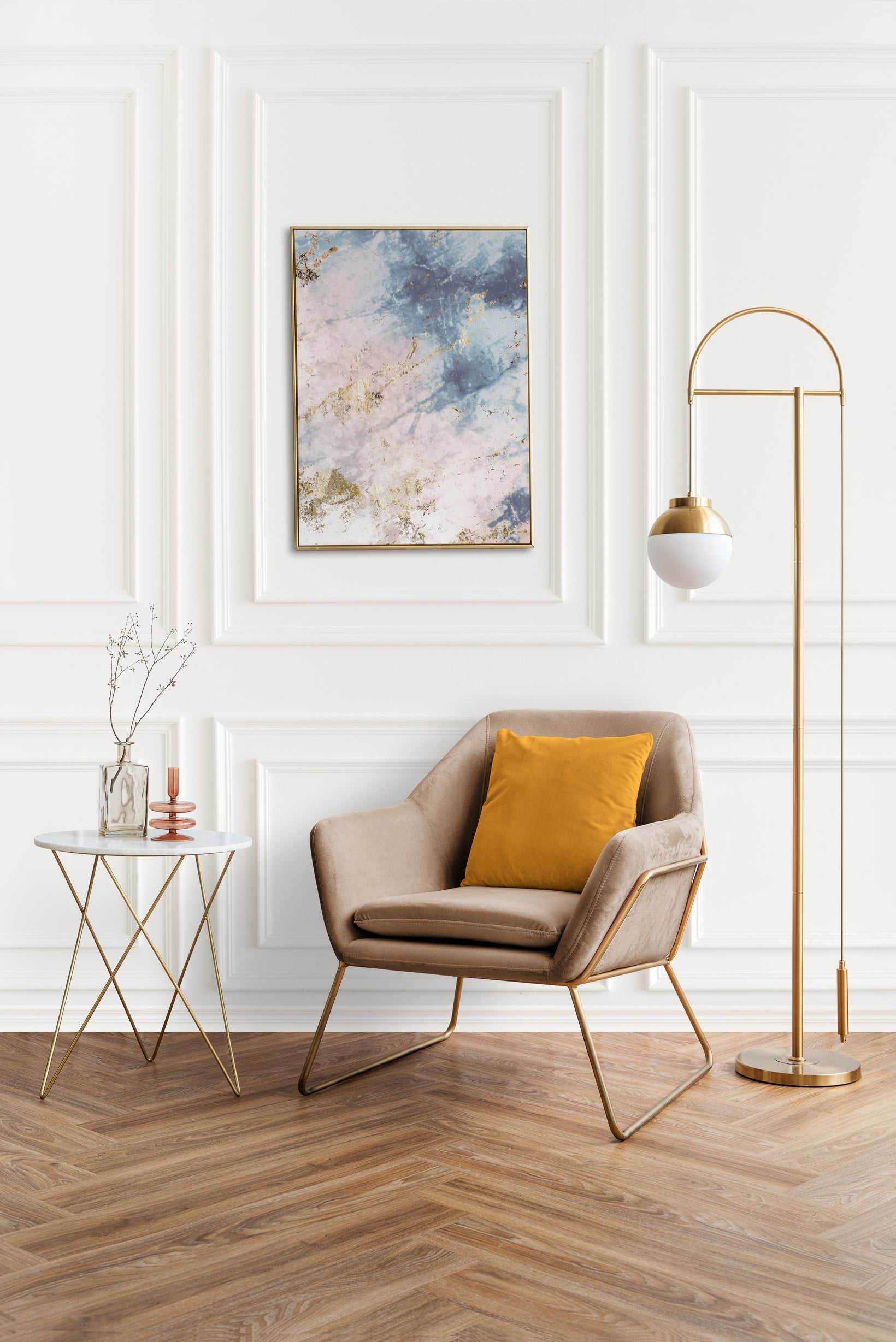 Modern interior with a beige armchair, gold side table, and floor lamp against a white wall with abstract art.

