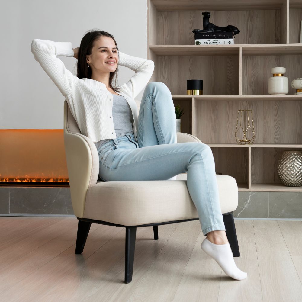 Woman sitting in a modern chair in a stylish room with shelves and a fireplace.

